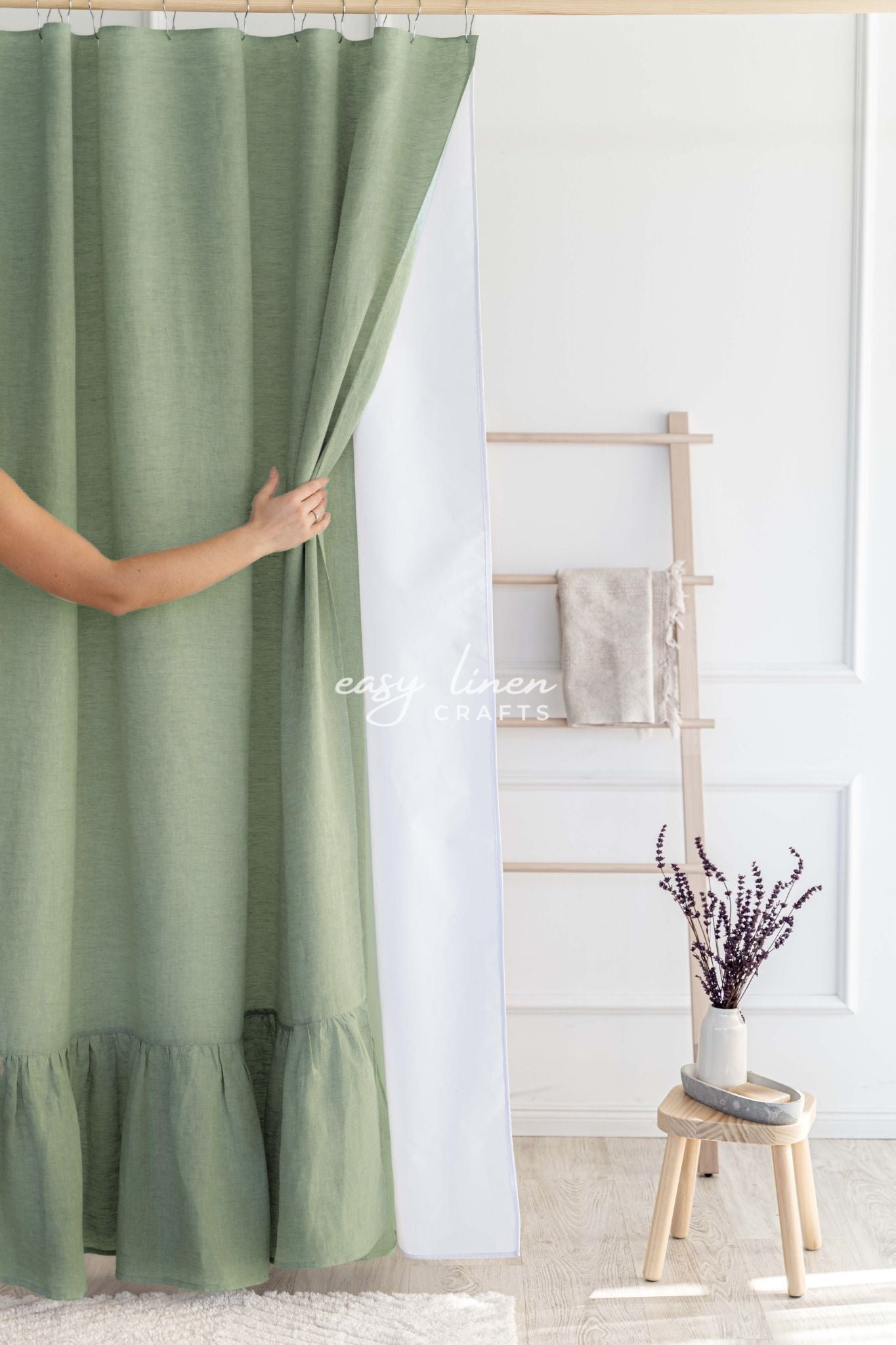 Khaki green linen shower curtain in a room with a white wall and a wooden stool.