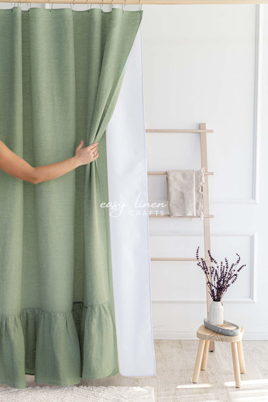 Khaki green linen shower curtain in a room with a white wall and a wooden stool.