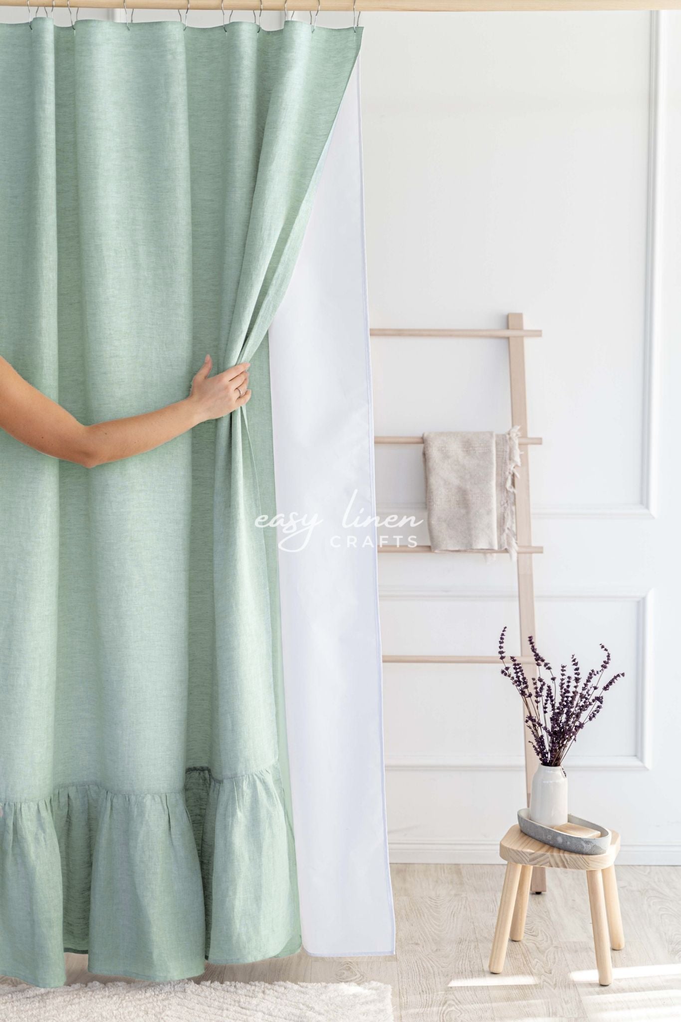Sage green shower curtain in a room with a white wall and wooden stool.