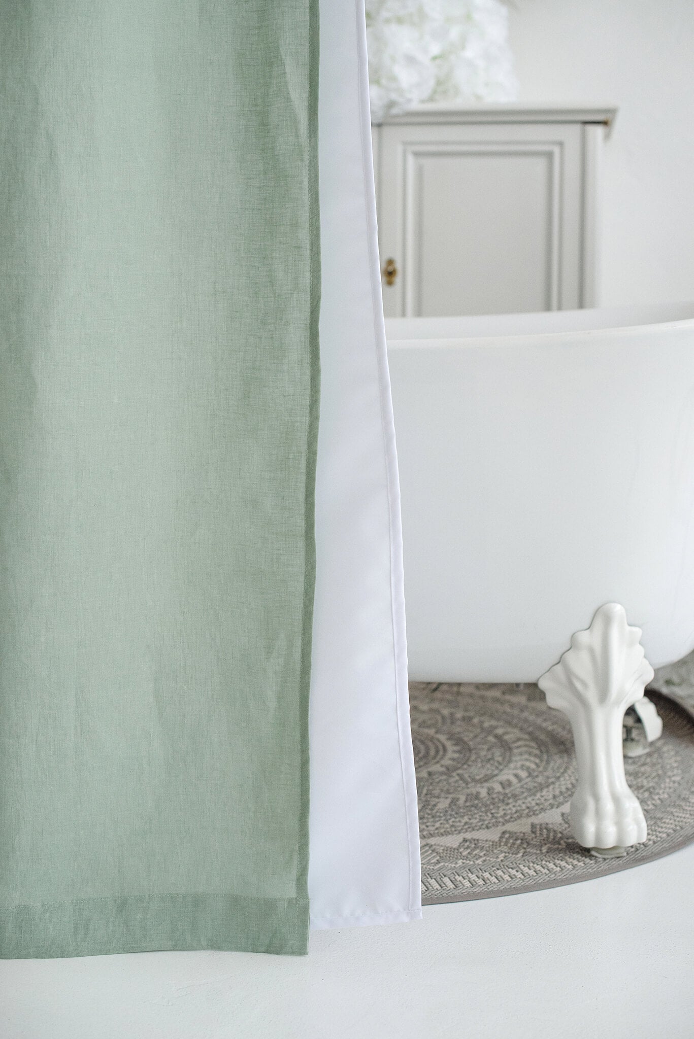 A sage green linen shower curtain with a white center stripe, hanging next to a white bathtub in a bright, modern bathroom setting.