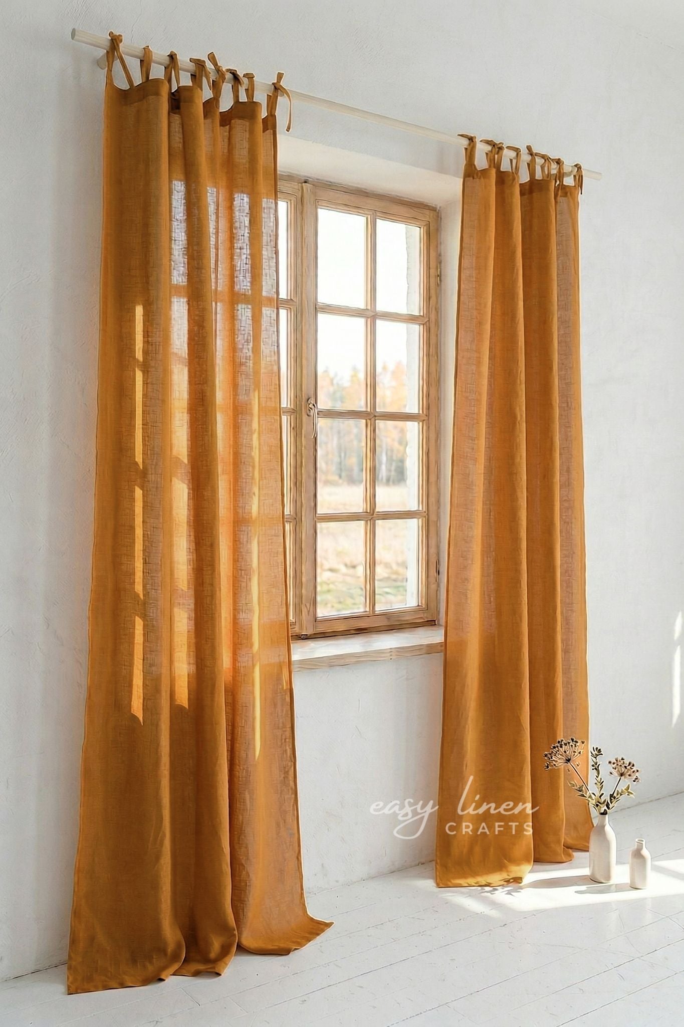Mustard yellow curtains hanging in front of a window with a white wall and small table with flowers in the background.