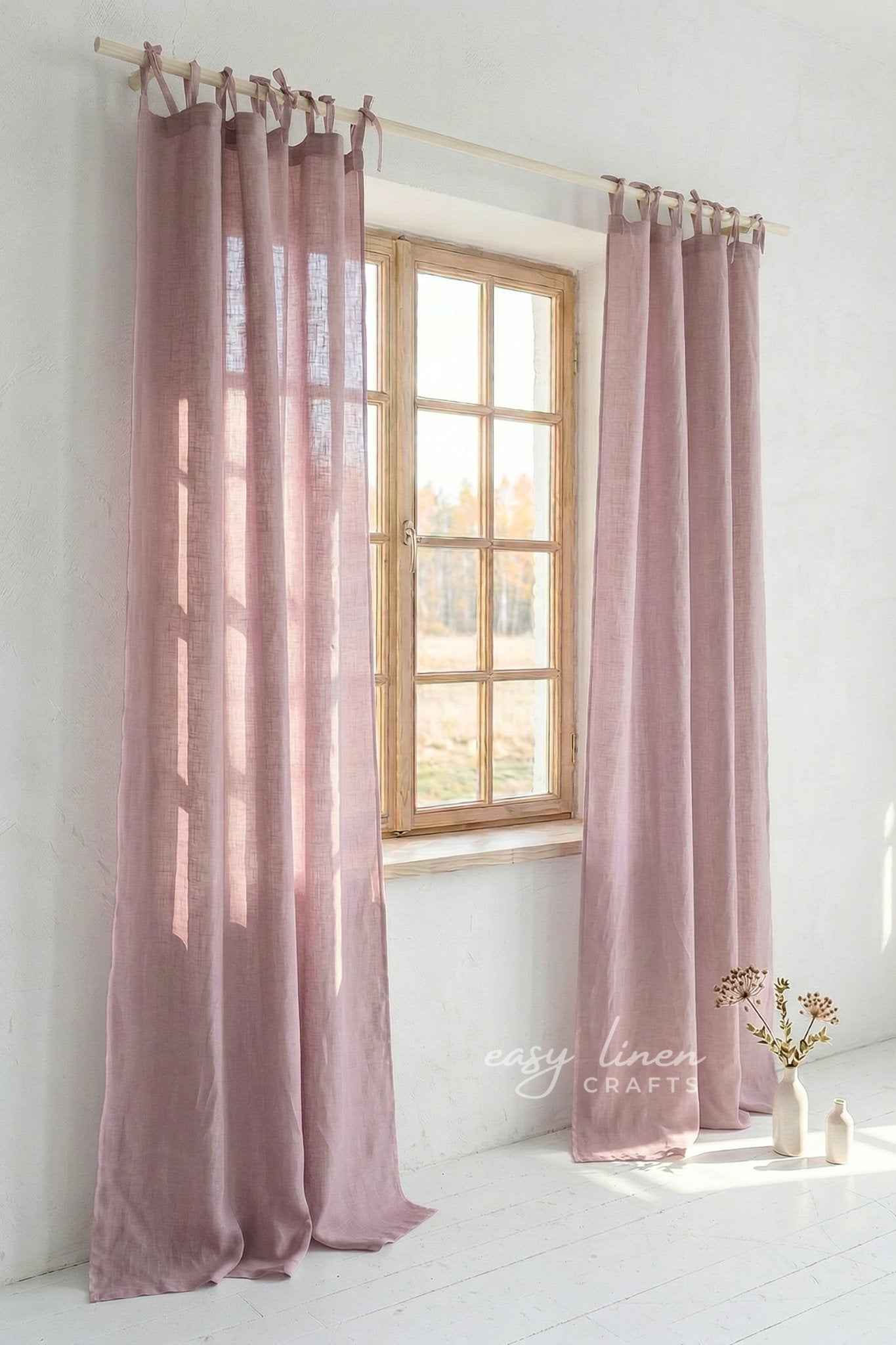 Pink curtains hanging in a window with a white wall and light floor.