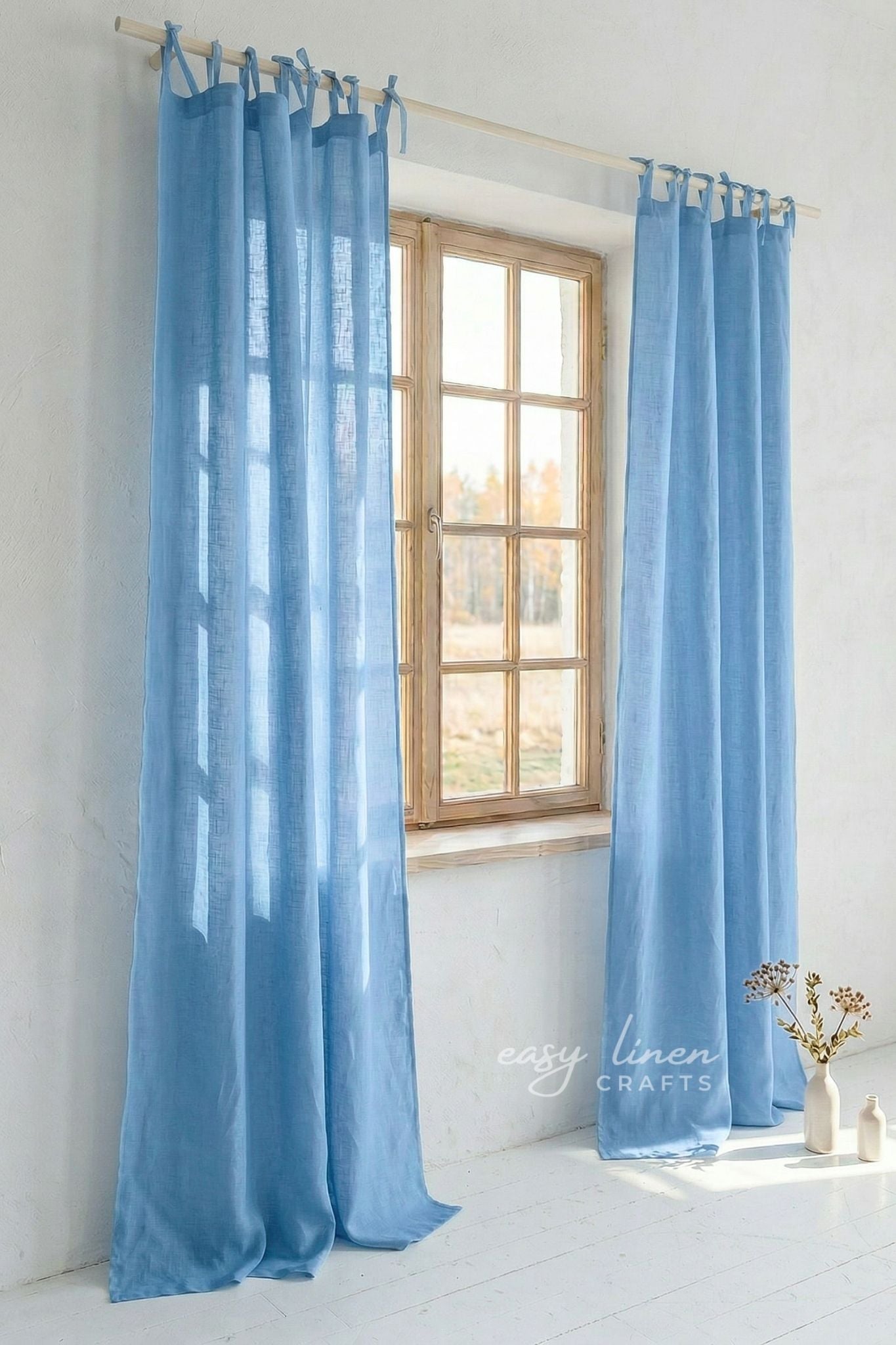 Light blue curtains hanging in front of a window with a white wall background.