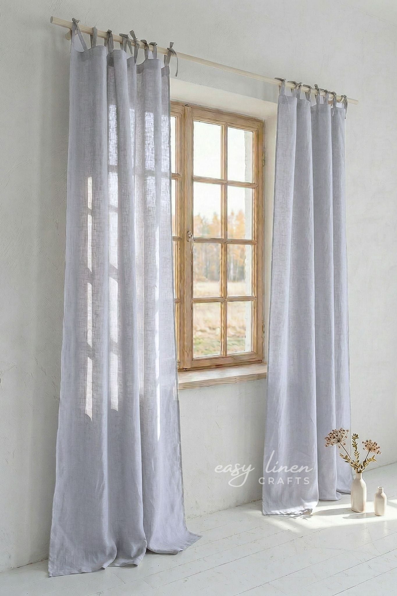 Light gray curtains hanging in front of a window with a white wall background.
