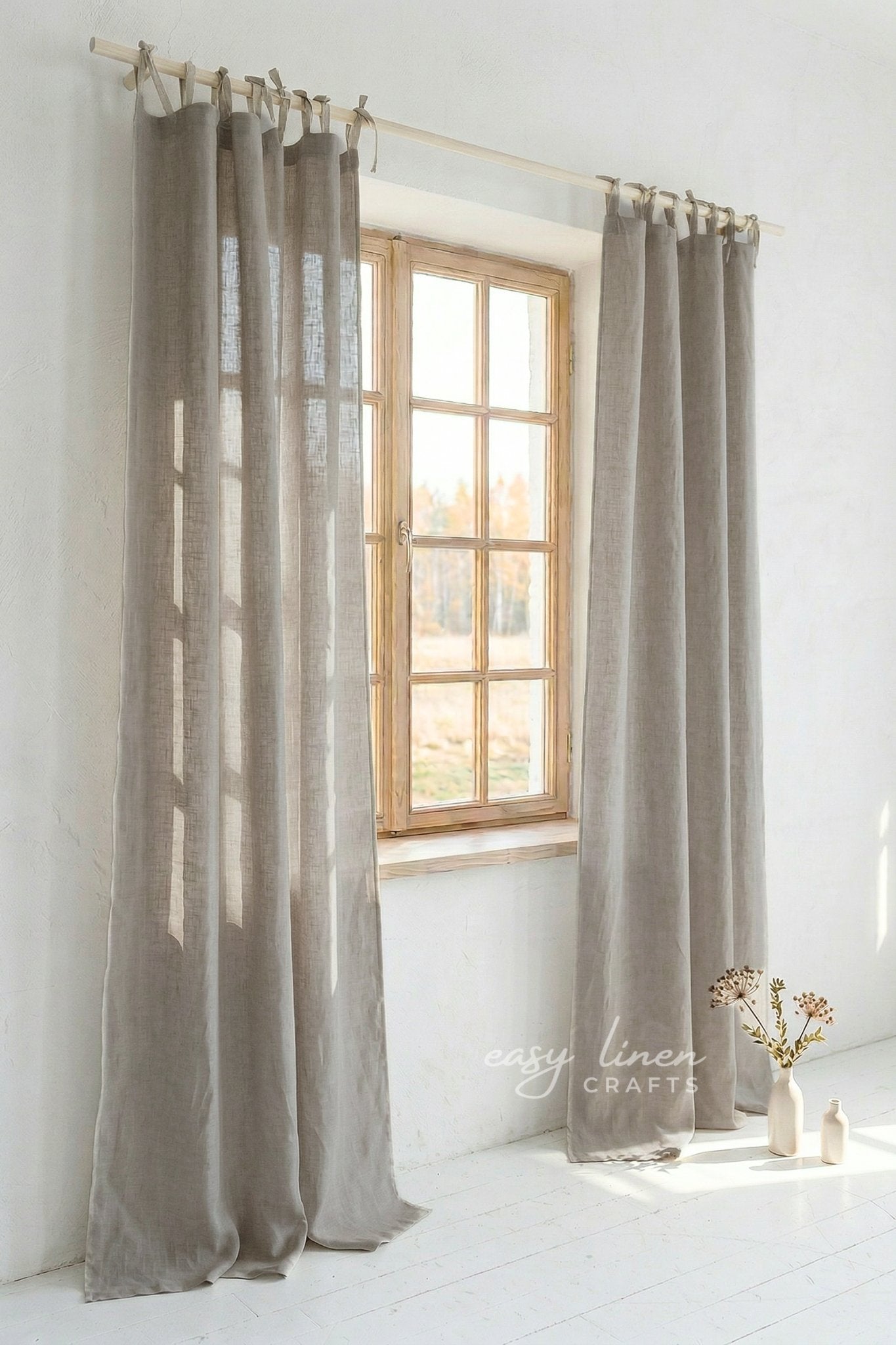 Pair of beige curtains hanging in front of a window with a white wall background.