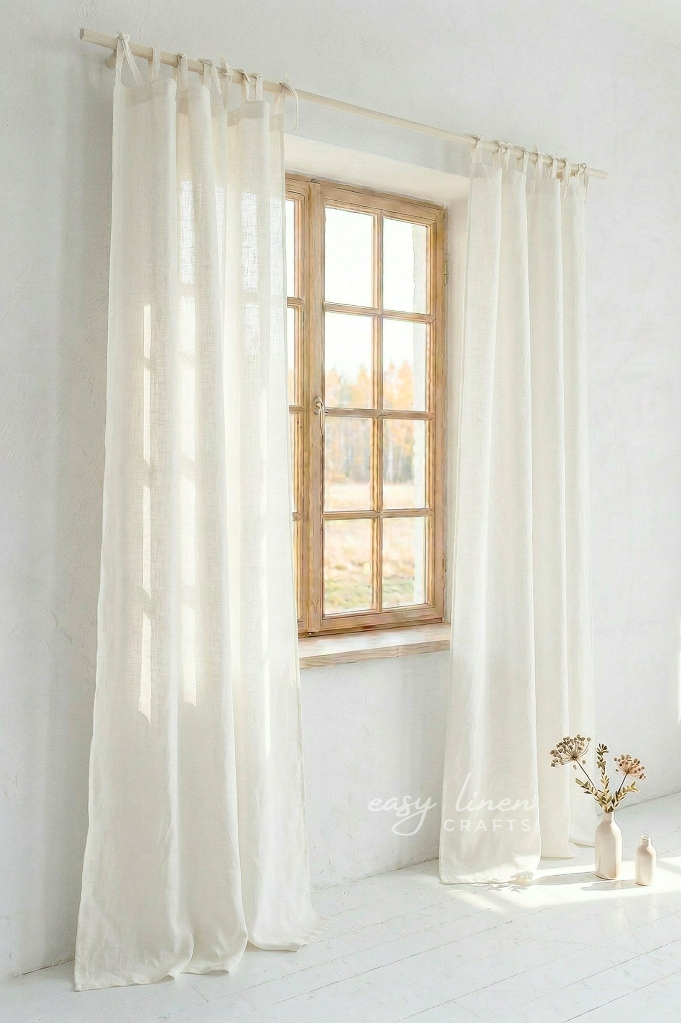 Ivory curtains hanging in front of a window with a minimal white room.