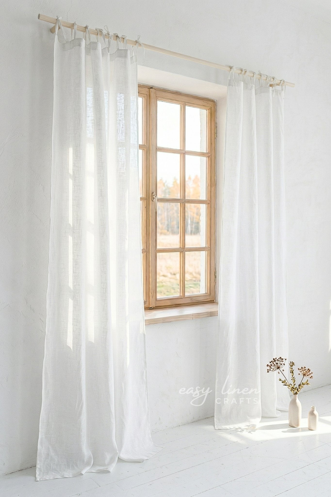 Sheer white curtains hanging in front of a window with natural light, on a white wall.